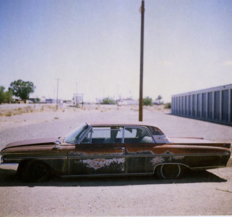 old car covered in rust abandoned at storage facility in desert