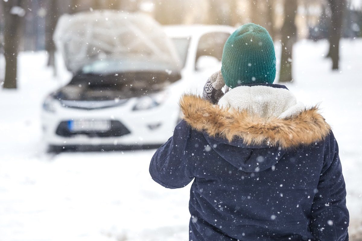person in winter attire calling for roadside assistance with their car hood up